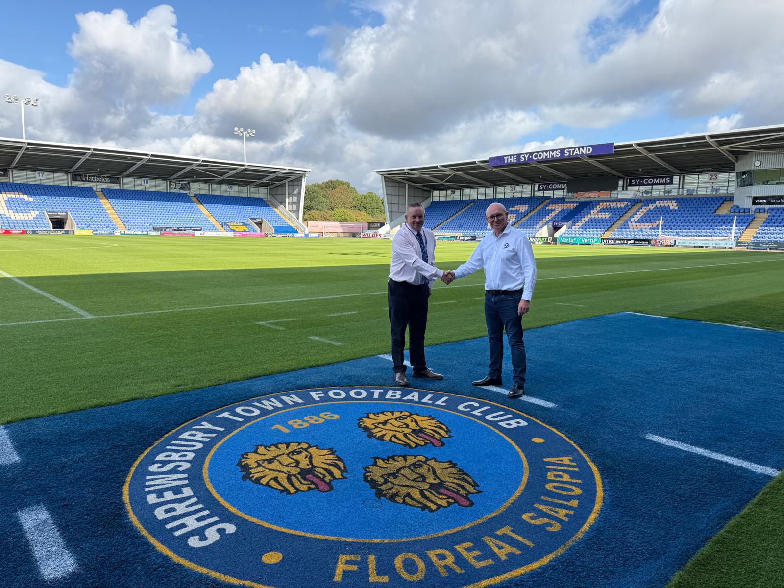 Two men shaking hands on a football pitch with Shrewsbury Town Football Club logo.